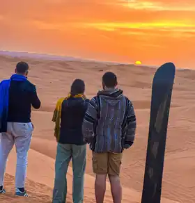 Three travellers watching the sunset over the Erg Chebbi dunes with a sandboard